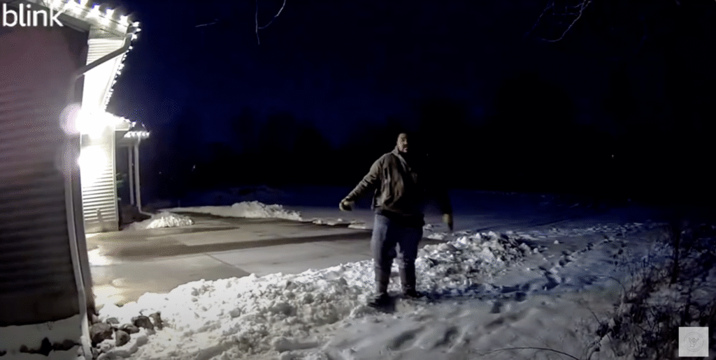 Person captured by Blink security camera at night in snowy front yard with motion spotlight activated